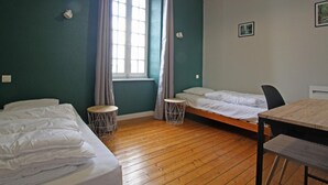 A room with two beds, a small round table, a chair, a window with curtains, and a ceiling light. - Comfortable cottage with WiFi and pets allowed (Périers)