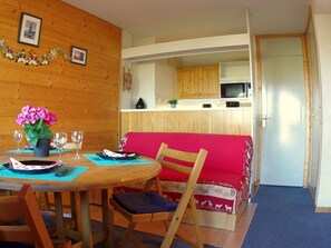 Una habitación acogedora con una mesa de comedor de madera, un sofá rojo y una zona de cocina con armarios de madera y un microondas.