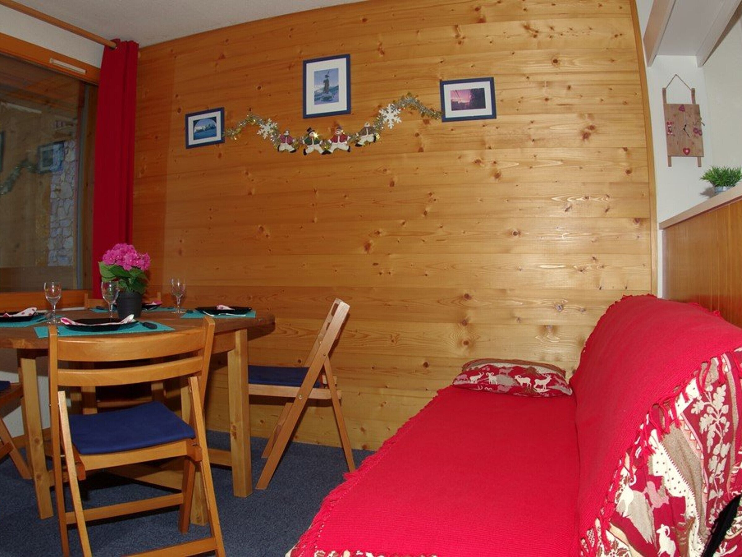 Um quarto aconchegante com paredes de madeira, uma mesa de jantar com cadeiras, um sofá vermelho e quadros na parede.
