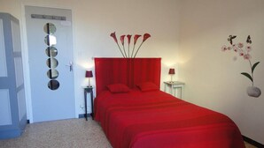 A bedroom with a red bedspread, a mirror on the door, and a wall-mounted orchid painting. - Cozy 2-Room Apartment, 300m from Beach with Terraces & A/C, Sleeps 4 (Port-la-Nouvelle)