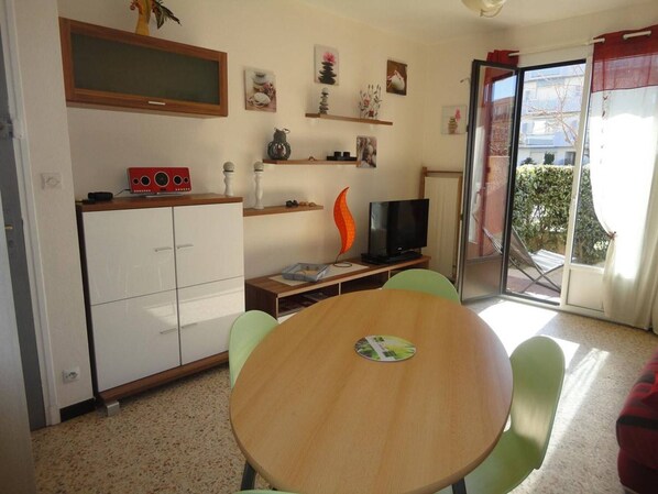 Espaço compacto com área de refeições, cozinha compacta e porta de vidro deslizante para uma varanda.