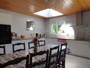 A modern kitchen with a dining area, featuring a skylight, a built-in oven, and a window with a view of greenery.