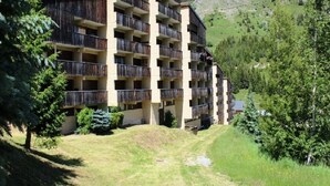 Un hôtel à plusieurs étages, doté de balcons, entouré de verdure et ayant une chaîne de montagnes en toile de fond.