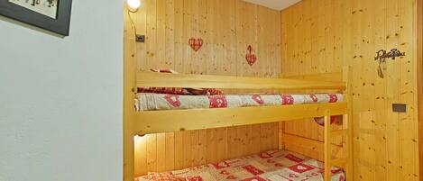 A bunk bed room with wooden walls, a framed picture, and a small light fixture.