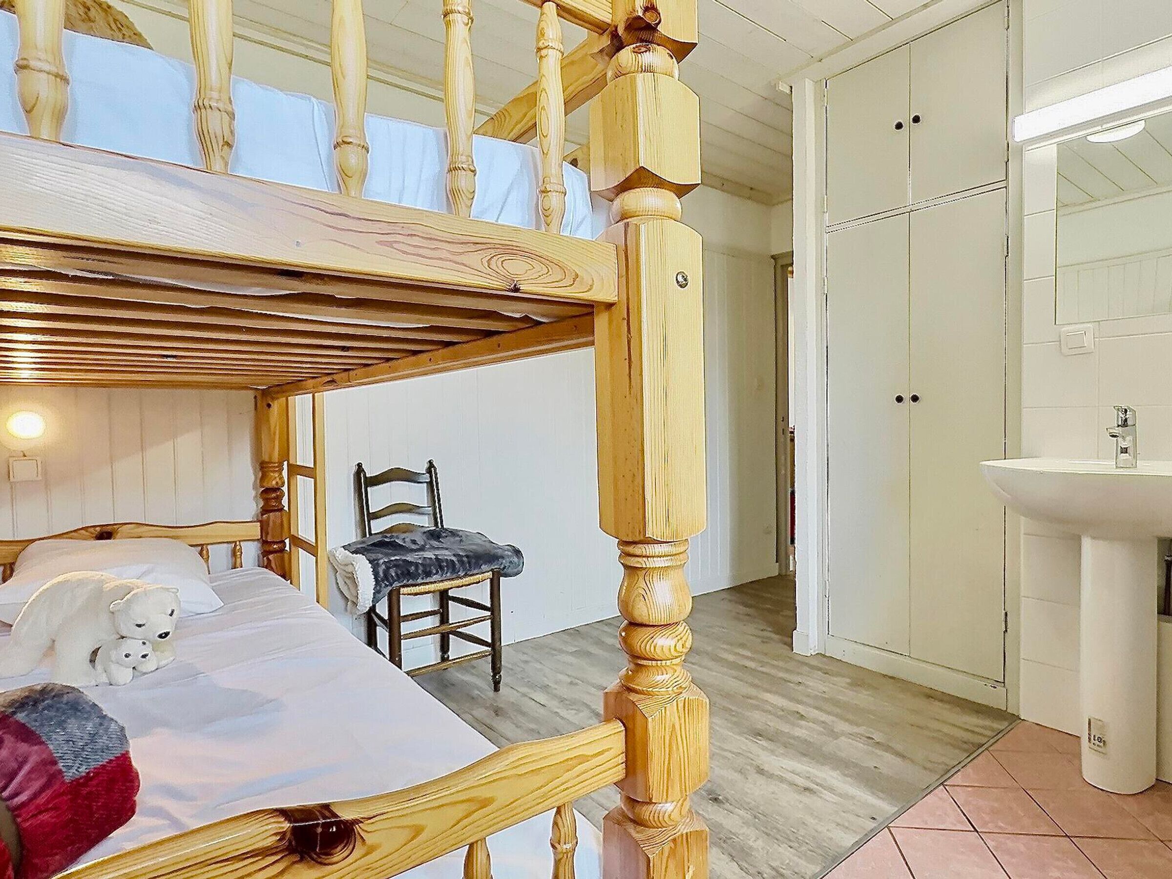 A room with a wooden bed, a chair, a wardrobe, and a bathroom with a sink.