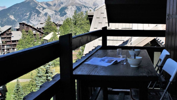 Ein Holzbalkon mit Tisch, Stühlen und Blick auf die Berge.