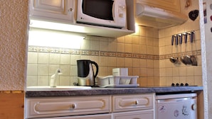 Eine Küche mit weißen Schränken, einer Mikrowelle, einer Kaffeemaschine und einem Kühlschrank.
