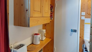 Une cuisine de taille réduite, avec des meubles en bois, un réfrigérateur blanc, un grille-pain et une bouilloire posés sur le plan de travail.
