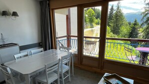 Una habitación con una mesa de comedor, sillas, una mesita con bandeja y vistas a un paisaje montañoso a través de grandes ventanales.
