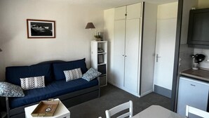 Un espacio habitable compacto con un sofá azul oscuro, una pequeña mesa de comedor y una zona de kitchenette.