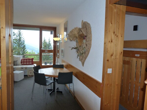 A room with a wooden table and chairs, a bench with a plaid cushion, and a large window with a view of trees and mountains.