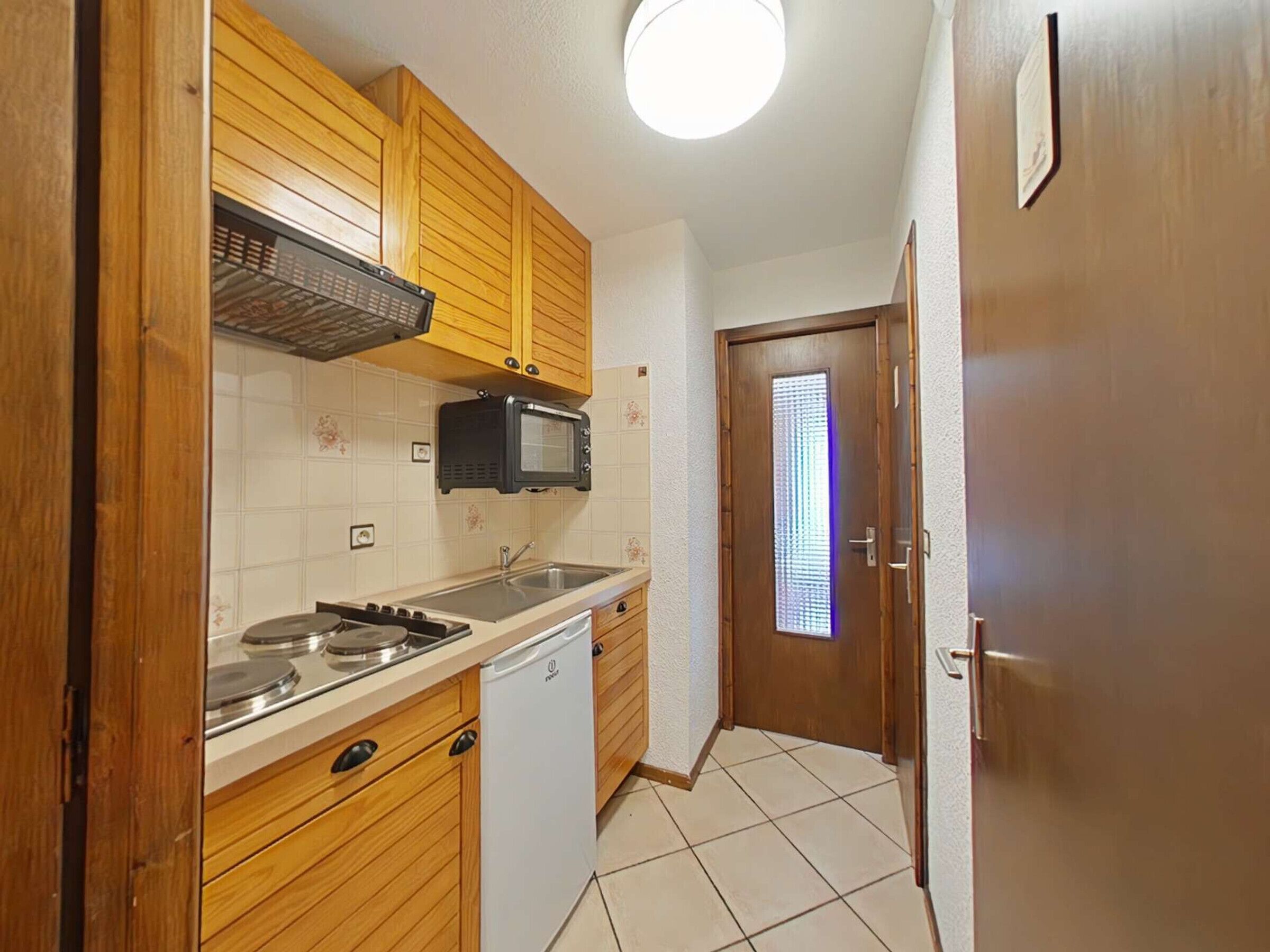 A compact kitchen with wooden cabinets, a microwave, a sink, and a dishwasher.