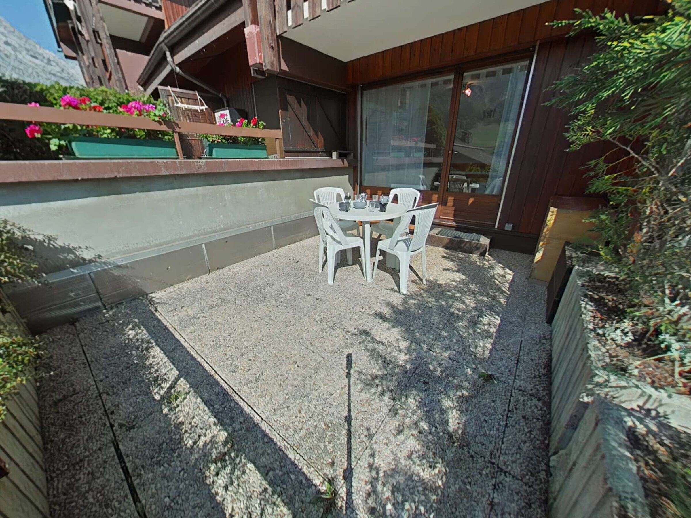 A patio with a table and chairs, surrounded by a wooden deck and a gravel area.