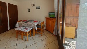Zona pranzo con tavolo imbandito per quattro persone, televisione su un mobile in legno e porta scorrevole in vetro che dà su uno spazio esterno.