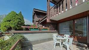 Un patio con tavolo e sedie, un pontile in legno e vista sulle montagne.