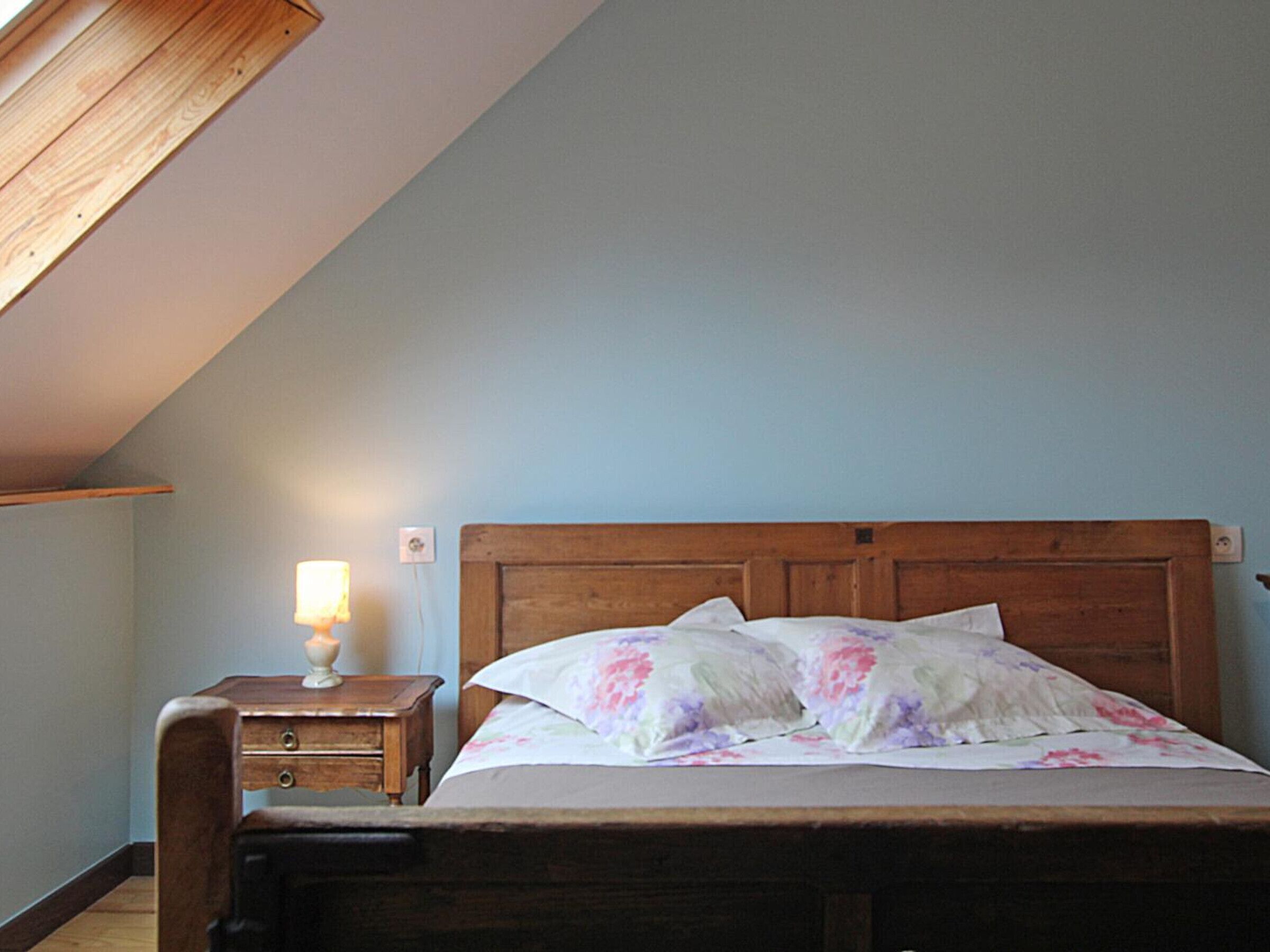 Ein Schlafzimmer mit einem hölzernen Bett, einem Nachttisch mit Lampe und einer schrägen Decke.