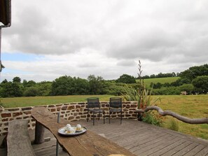 Une terrasse en bois avec une table et des chaises, donnant sur un champ verdoyant et un mur de pierres.