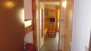 A narrow hallway leading to a room with a bed, a small table, and a door. - Studio cabin for 4, covered parking, 50m from slopes (La Mongie)