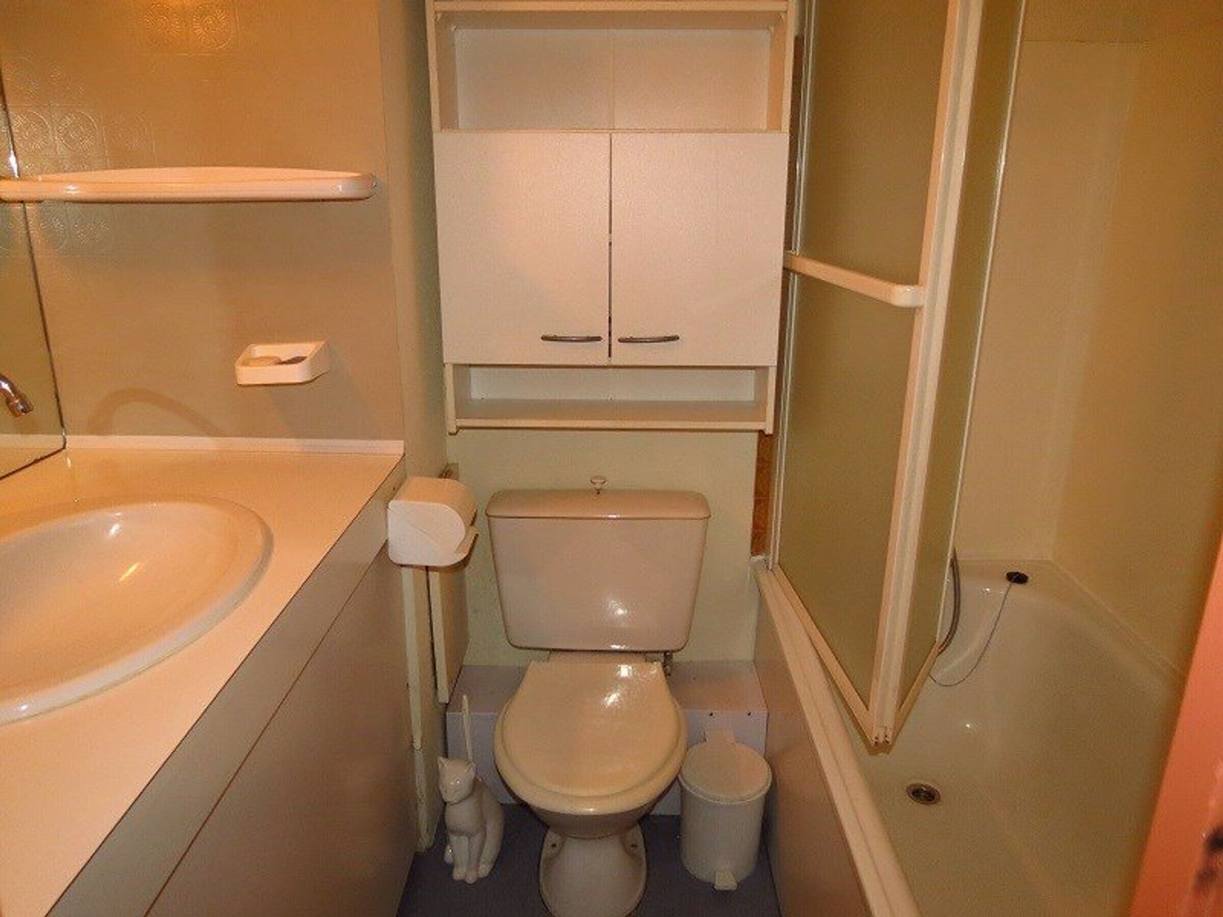 A small bathroom with a toilet, sink, and storage cabinet.