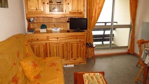 A compact living space with a wooden kitchenette, a sofa, a small table, and a view through a glass door. - Studio cabin for 4, covered parking, 50m from slopes (La Mongie)