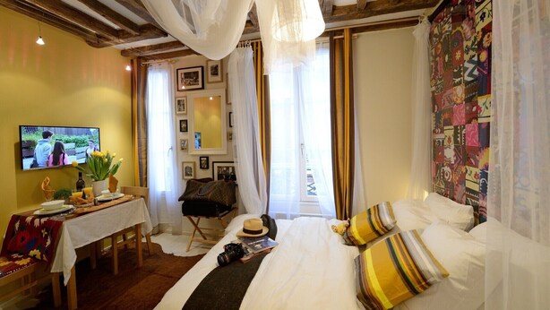 Une chambre d’hôtel comprenant un lit, un bureau avec une chaise, une télévision et une fenêtre avec des rideaux.