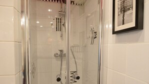 Une douche fermée par des parois en verre, dotée d’un pommeau de douche à main, d’un porte-serviettes fixé au mur et d’un tableau encadré accroché au mur.
