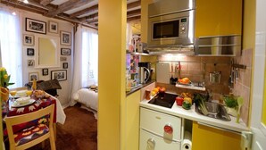 Une cuisine équipée d’un four à micro-ondes, d’une cuisinière et de divers ustensiles de cuisine. On y trouve également un coin repas avec une table dressée pour deux personnes, et un lit à l’arrière-plan.