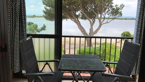 A balcony with a table and two chairs, overlooking a lake and trees.