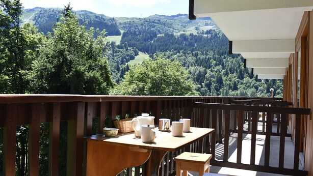 A balcony with a wooden table and chairs, overlooking a forested valley. - Central ski-in apartment - 5 guests (Méribel)