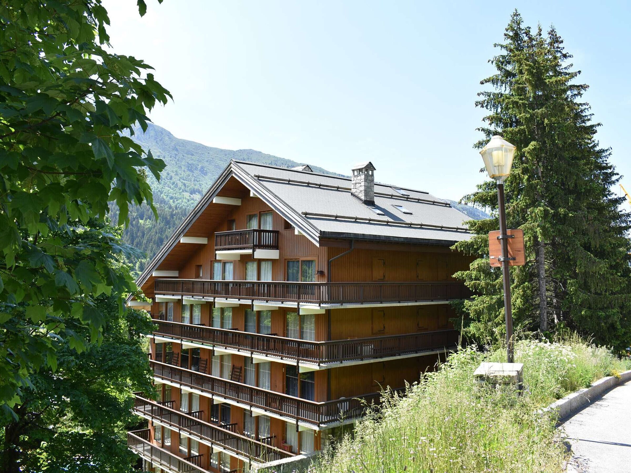 A multi-story wooden building with balconies, surrounded by greenery and mountains.