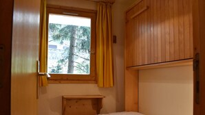 A small, single-bed room with a window, wooden wardrobe, and a small wooden shelf. - Central ski-in apartment - 5 guests (Méribel)