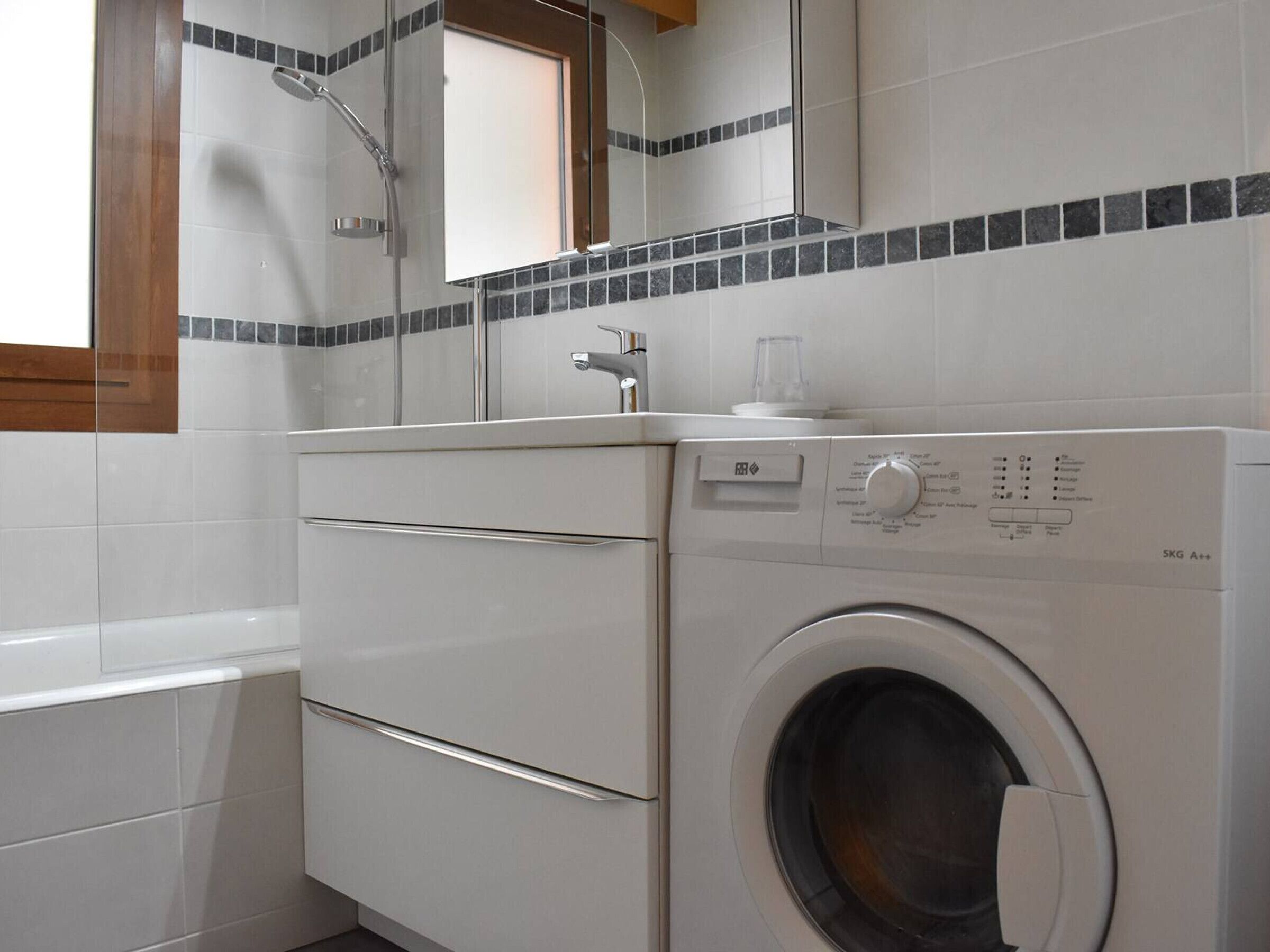 Ein kompaktes, modernes Badezimmer mit Waschmaschine, Spiegel und Duschbereich.