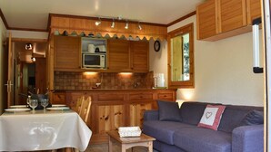 A compact kitchen with wooden cabinets, a microwave, and a dining area with a table set for two. - Central ski-in apartment - 5 guests (Méribel)