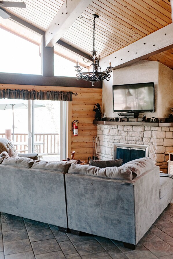 A cozy living room with a large sectional sofa, a fireplace, a television, and a wooden ceiling.