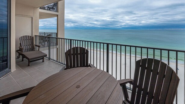 Een balkon met uitzicht op de oceaan, een ronde houten tafel en twee Adirondack stoelen.