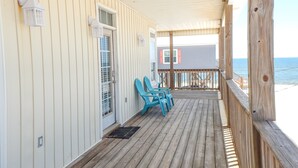 Een houten terras met uitzicht op de oceaan, een deur met raam, en twee blauwe stoelen.