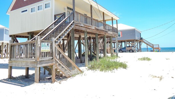 Een houten strandhuis met een balkon en een trap naar de ingang.