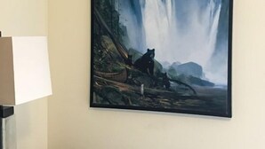Habitación con un cuadro grande de una cascada y osos en la pared, un escritorio negro y una lámpara.