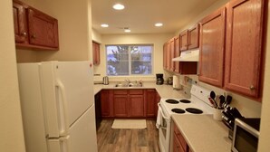Una cocina compacta con armarios de madera, un refrigerador blanco, una estufa y un microondas.