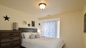 Un dormitorio con cama, cómoda, decoraciones en la pared y ventana con persianas.