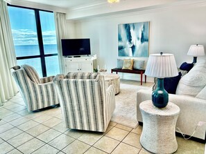 A living room with a large window, a flat-screen TV, a sofa, a coffee table, and a lamp. - 2 BR/2.5 BA Condo on the 10th Floor! In Walking Distance to Flora Bama! (Orange Beach)
