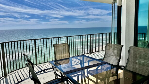 A balcony with a glass table and chairs, overlooking the ocean.