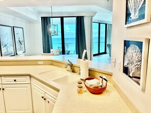 A kitchen with a large window, a sink, and a countertop with a basket containing towels and jars. - 2 BR/2.5 BA Condo on the 10th Floor! In Walking Distance to Flora Bama! (Orange Beach)