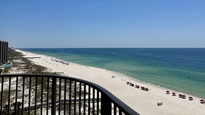 A beach with white sand, clear blue water, and a few umbrellas.