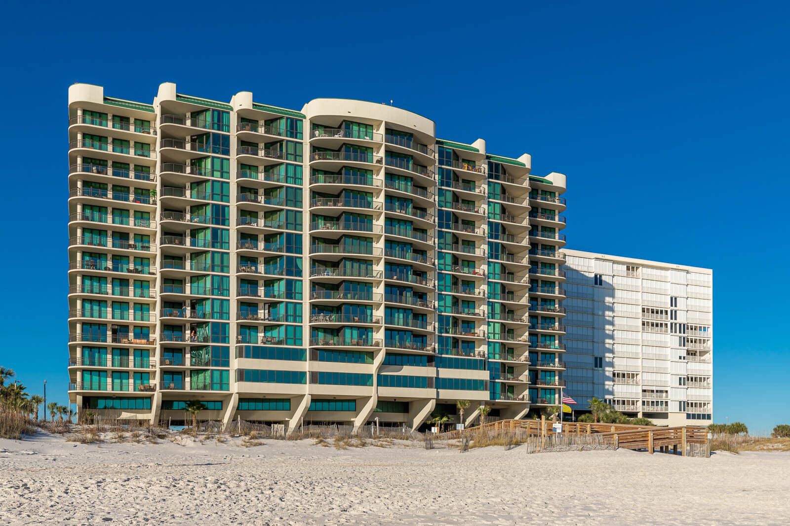 A multi-story hotel with balconies, located on a sandy beach.