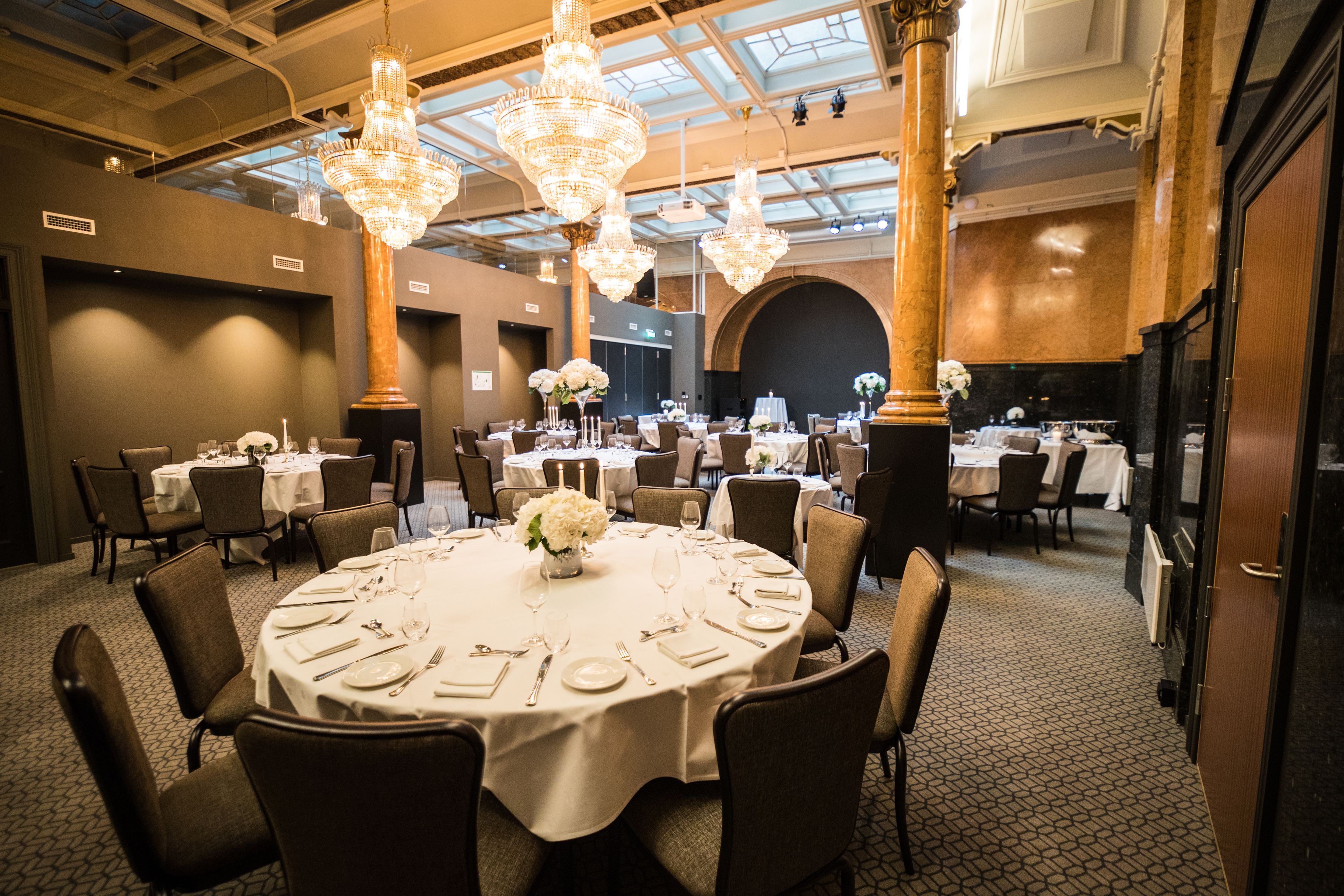 A banquet hall with round tables, chandeliers, and a high ceiling with skylights.