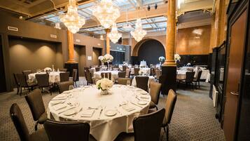 A banquet hall with round tables, chandeliers, and a high ceiling with skylights.