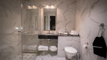 Ein modernes Badezimmer mit einer Duschkabine aus Glas, einem marmorverlegten Boden, einem schwarzen Waschtisch und einer weißen Toilette. Ein Handtuchhalter mit Handtüchern ist ebenfalls vorhanden.