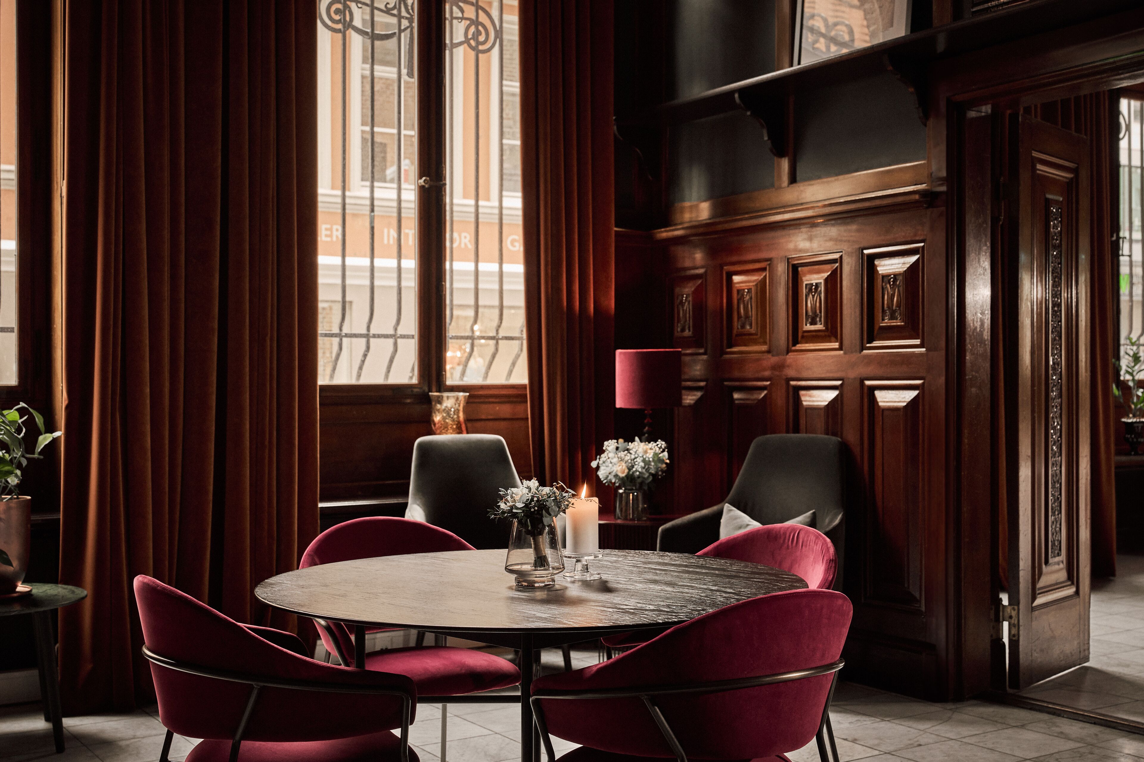 A dining area with a round table, red upholstered chairs, a candle, and a vase with flowers.