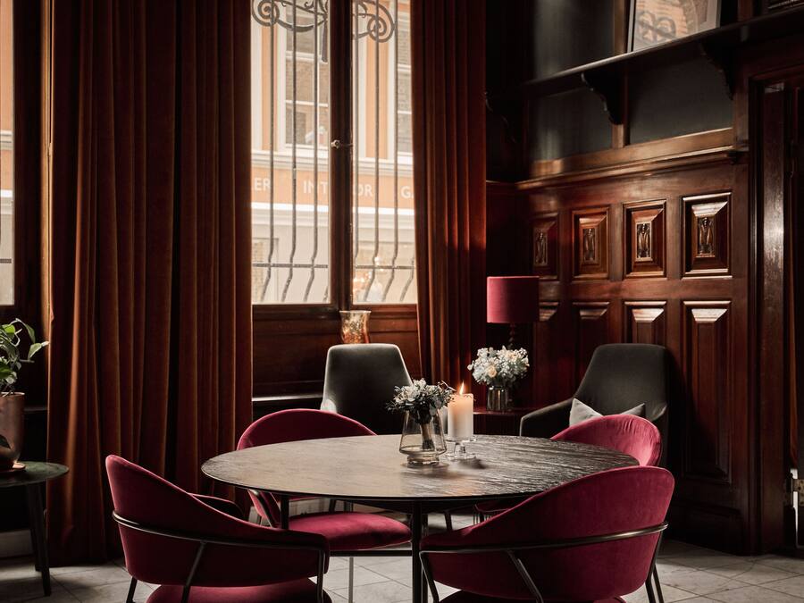 A dining area with a round table, red upholstered chairs, a candle, and a vase with flowers.